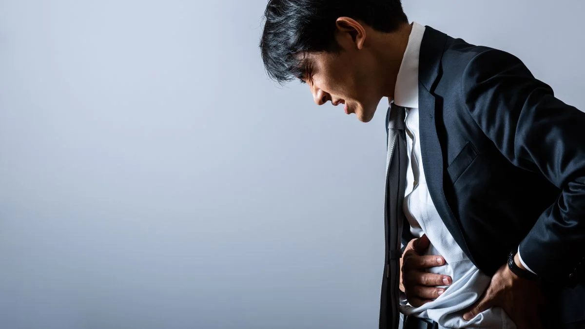 スーツ姿の男性が腹部を押さえてうずくまる。IBSの腹痛のイメージ