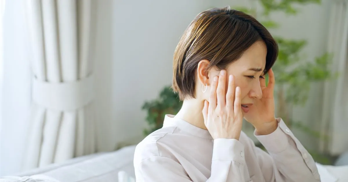 こめかみに手を当てて頭痛に悩む女性