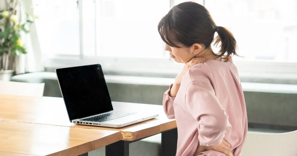 肩と腰の痛みを感じながらデスクワークをする女性