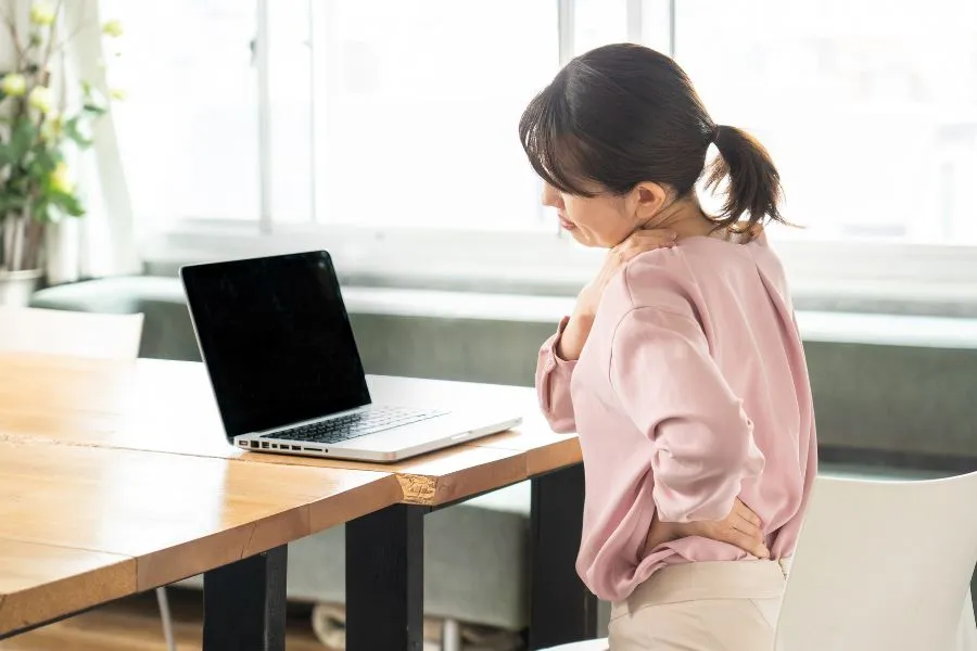 肩と腰の痛みを感じながらデスクワークをする女性
