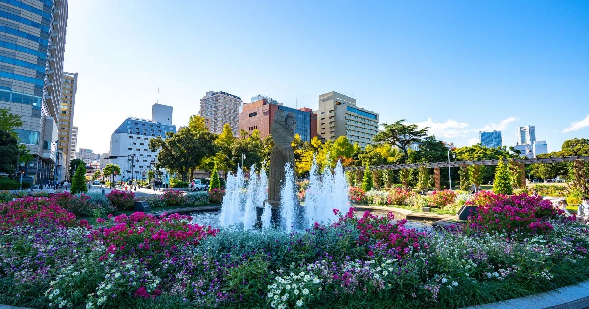 山下公園の噴水と色とりどりの花壇、奥にはライオンズプラザ山下公園や中華街方面の街並み