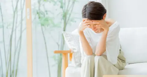 片頭痛の発作で頭を抱え、つらそうに座っている女性