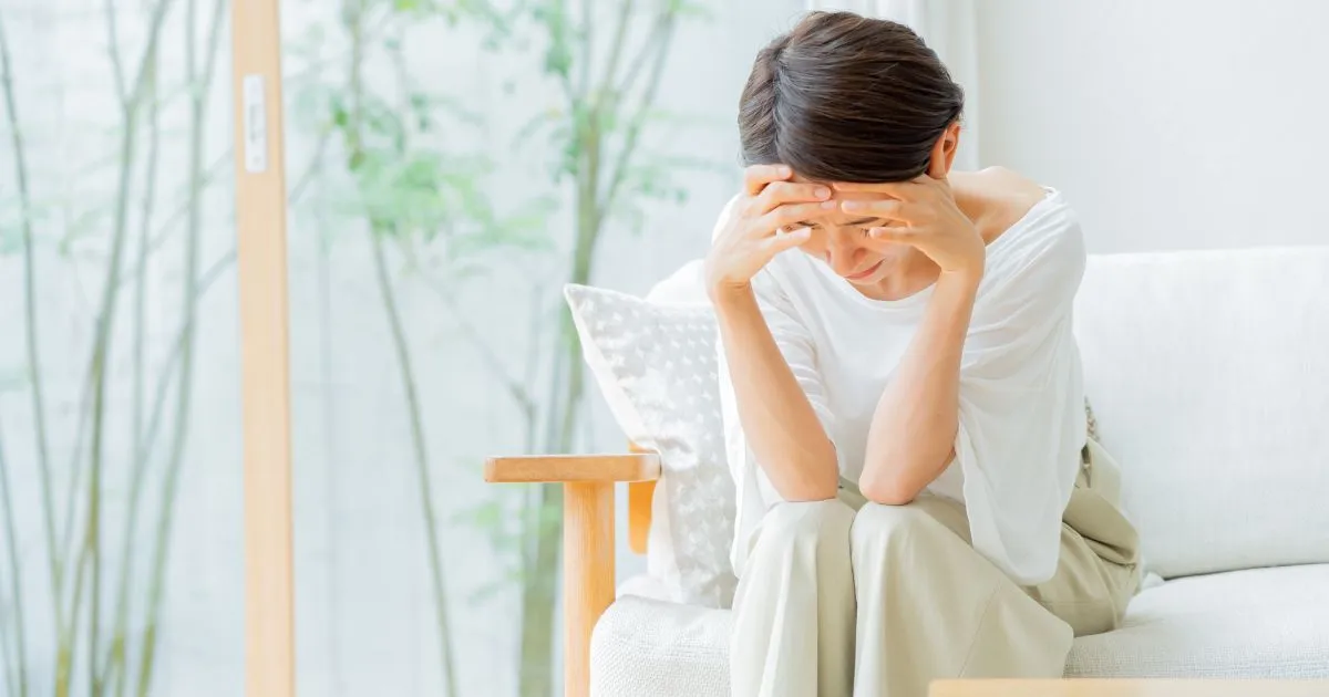 片頭痛の発作で頭を抱え、つらそうに座っている女性