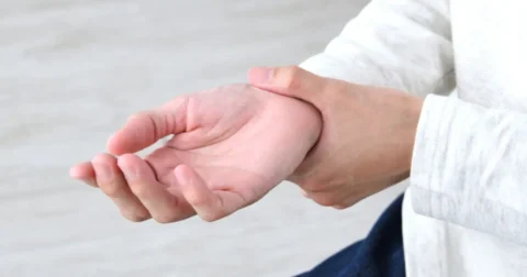 手首を押さえ、手のしびれや違和感を感じている様子